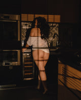 Lady standing in a dimly lit kitchen with a focus on their lower body.