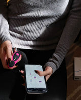 A person wearing a gray sweater holds a smartphone with the Ferri app-controlled panty vibrator, ready for some long-distance playtime.