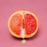 Halved grapefruit with creamy liquid on pink background, styled suggestively for bold, sensual fruit or food photography.