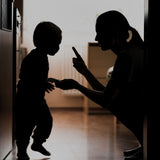 Backlit silhouette of a parent crouching and gently scolding a young child in a hallway, conveying discipline, guidance, and a serious family moment.