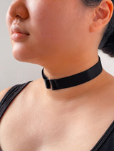 Close-up of a person wearing a black choker necklace against a neutral background