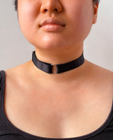 Person wearing a black choker necklace against a neutral background