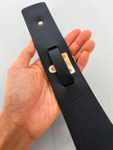Hand holding a black leather collar with gold hardware