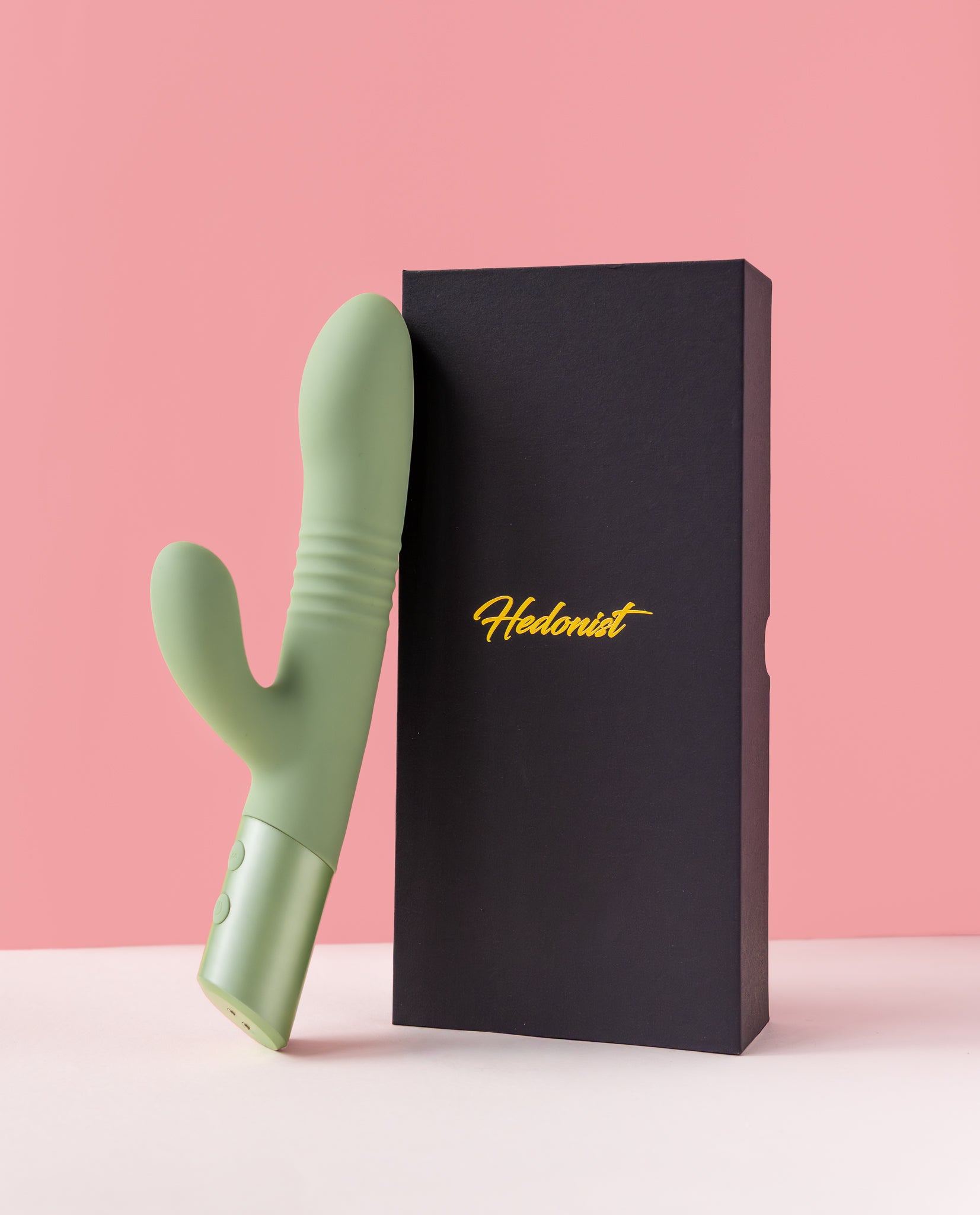 green mystique thruster rabbit vibrator next to a black box with 'Hedonist' branding on a pink background