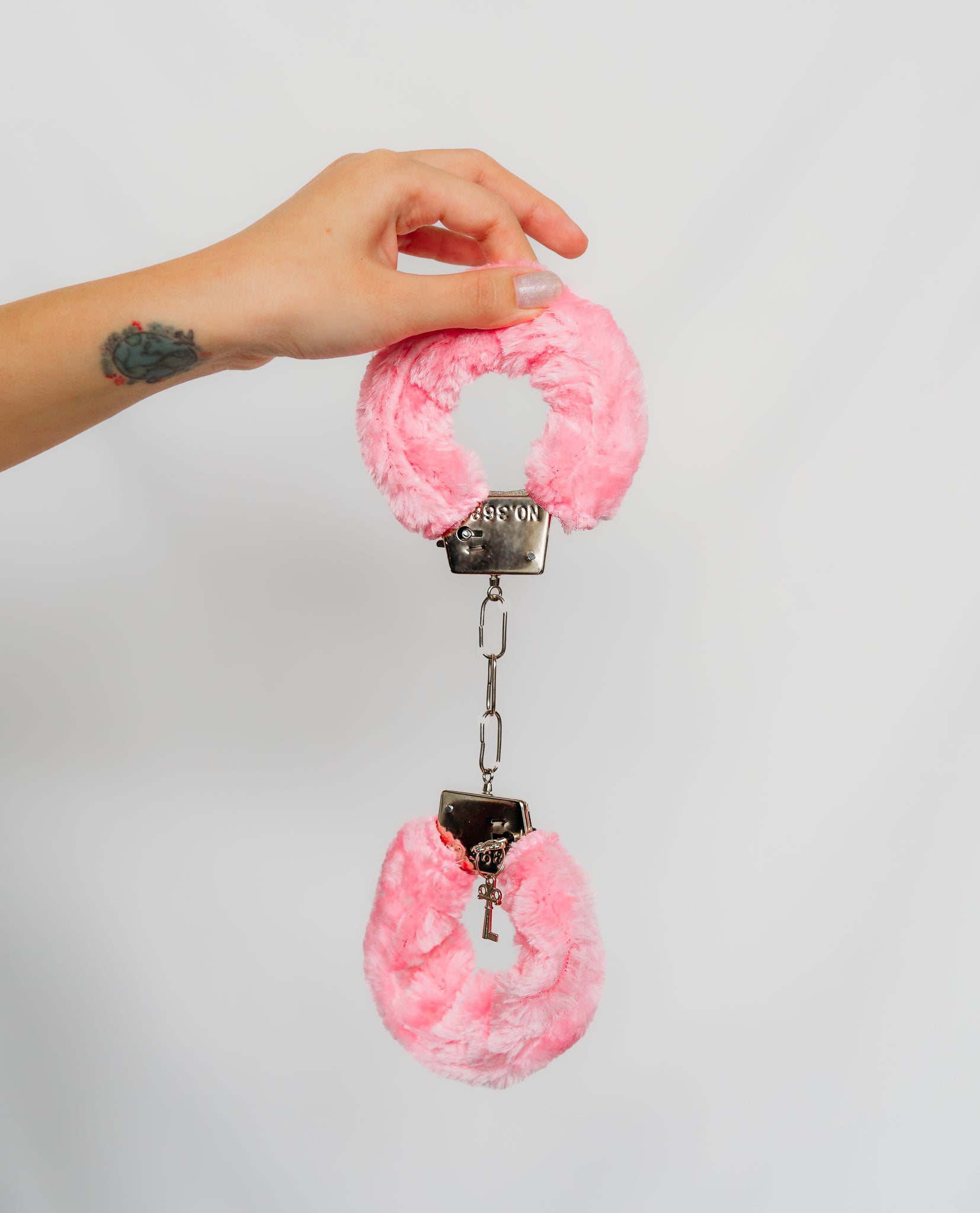 Pink furry cuffs with metal keychain on a plain background