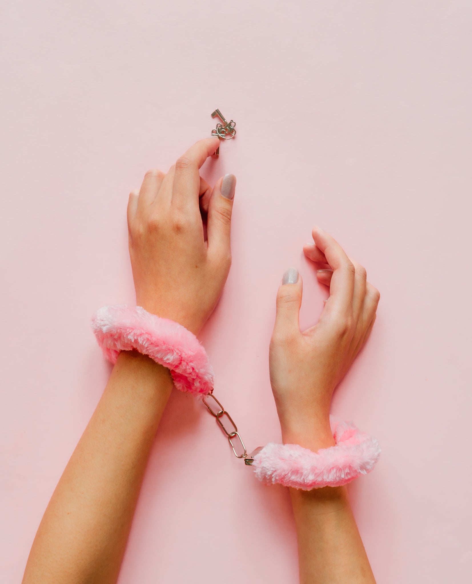 Hands with pink furry cuffs on a pink background
