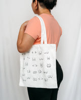 Person holding a white tote bag with black boobs and butt illustration 
