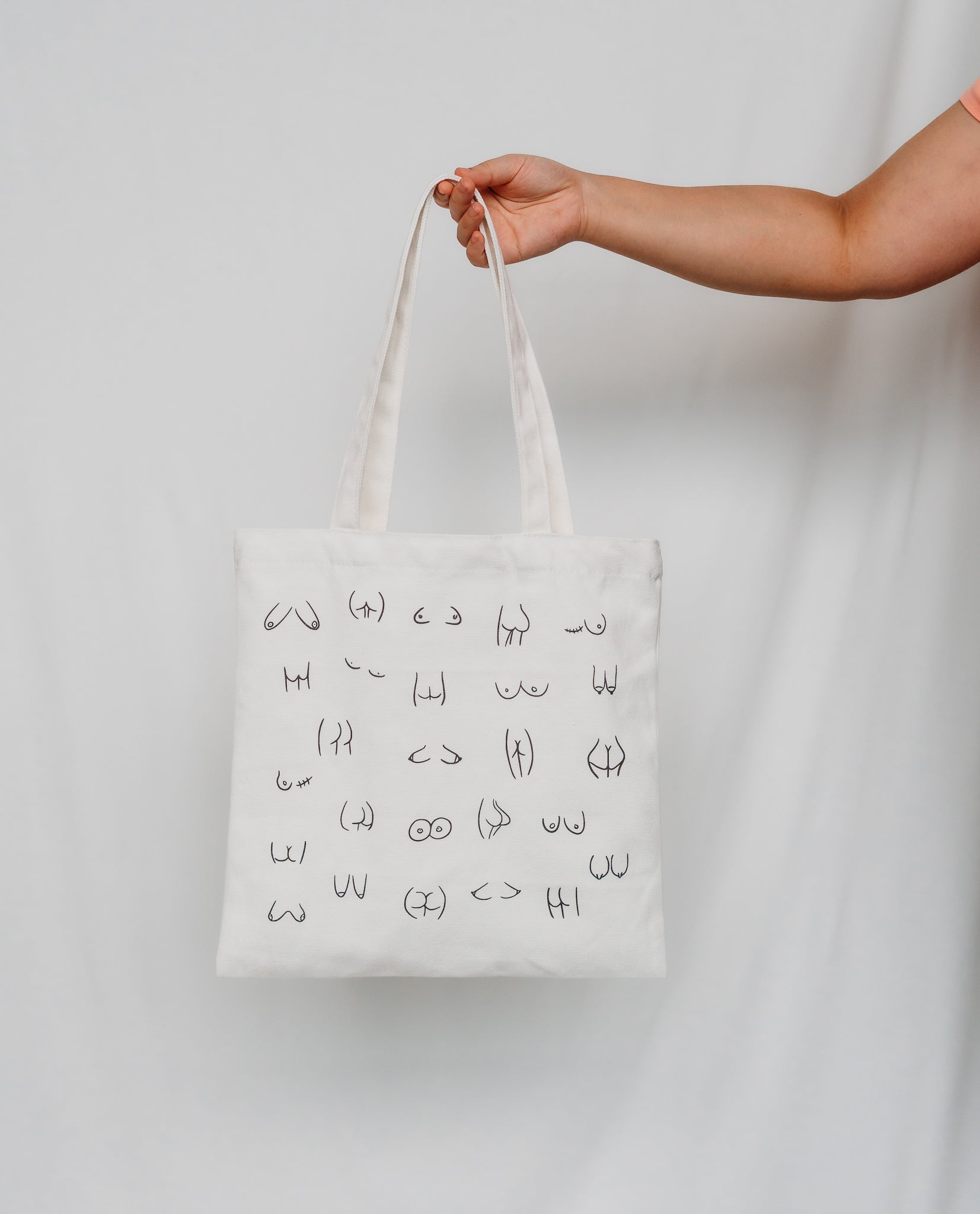 Person holding a white tote bag with black boobs and butt illustration 