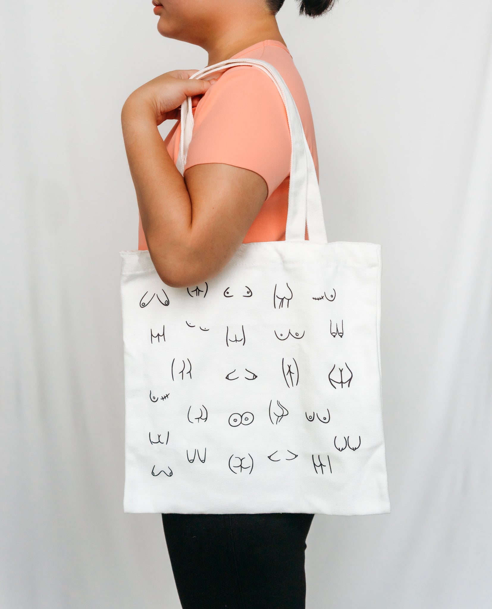 Person holding a white tote bag with black boobs and butt illustration 