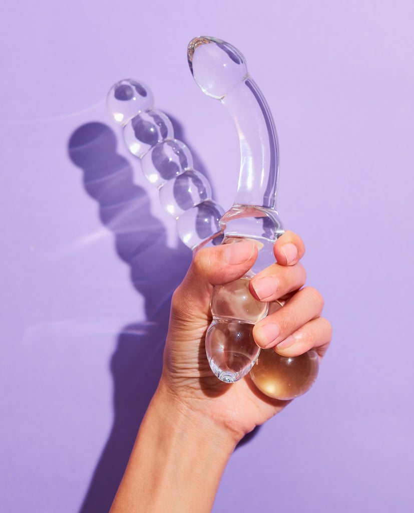 Hand holding transparent bubble wand glass dildo and curved glass dildo, female empowerment
